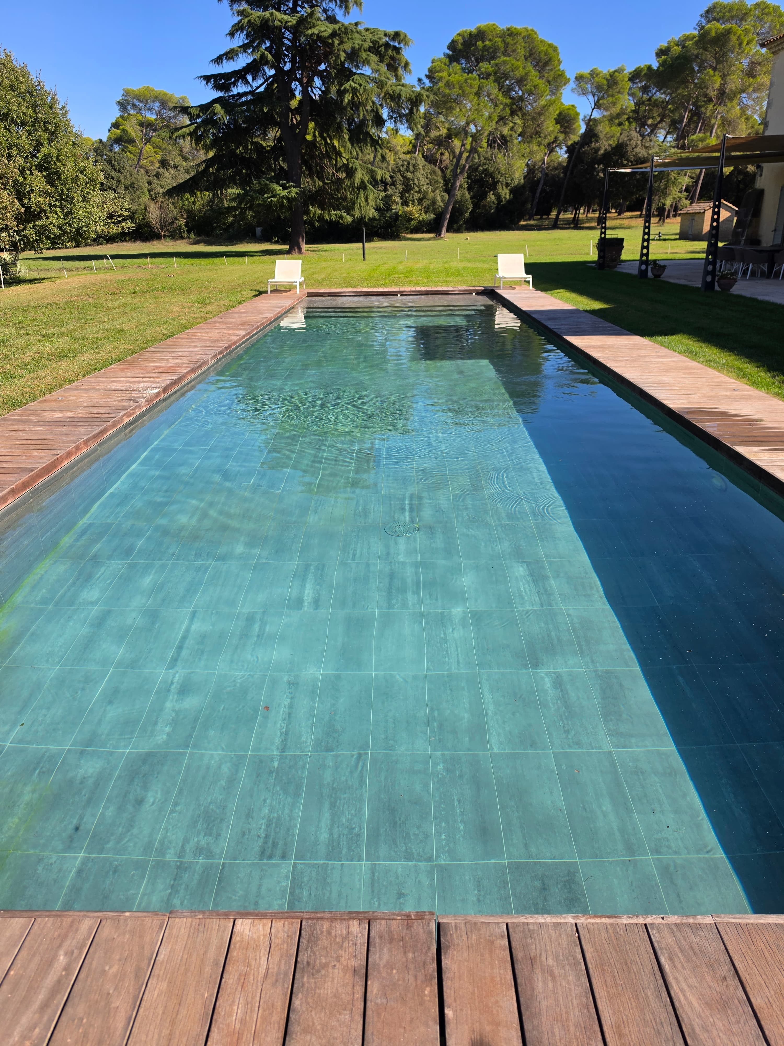 Piscine bordée d'une terrasse en bois, sous les grands arbres