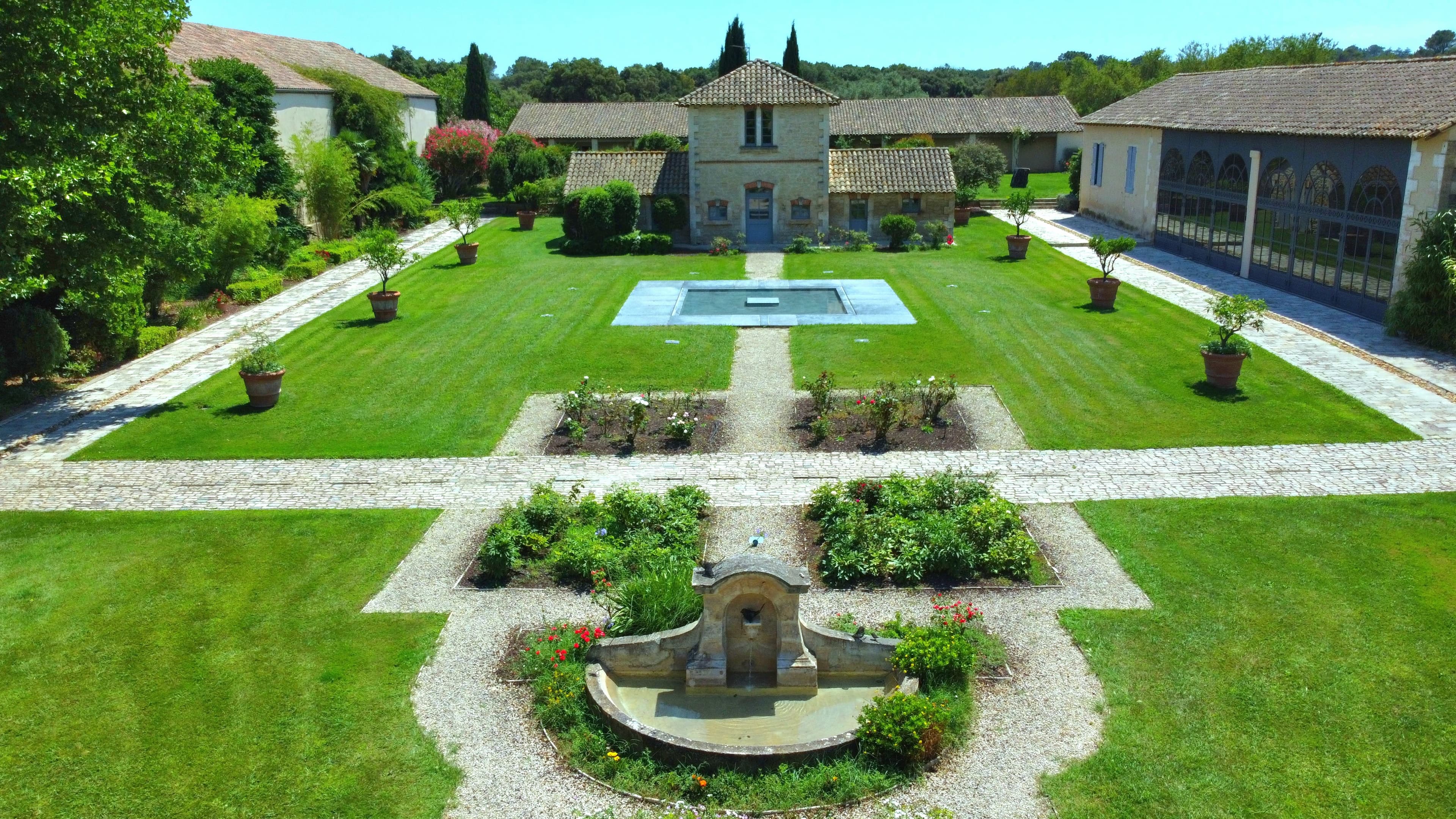 Cour du domaine avec bassin, allées pavées et massifs de rosiers