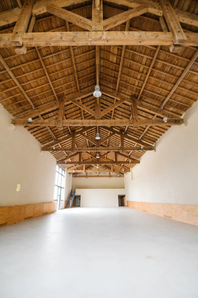 Grande salle de réception vide sous une charpente en bois, éclairée par une verrière