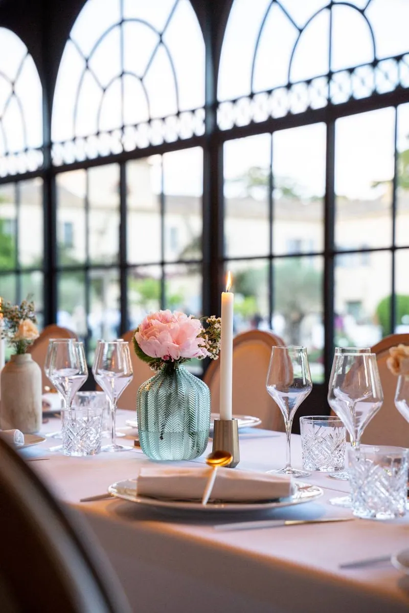 Table dressée devant des verrières en arcades, avec pivoine rose et bougie