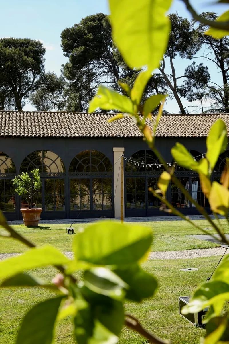 Bâtiment aux verrières en arcades vu depuis la pelouse, sous les pins