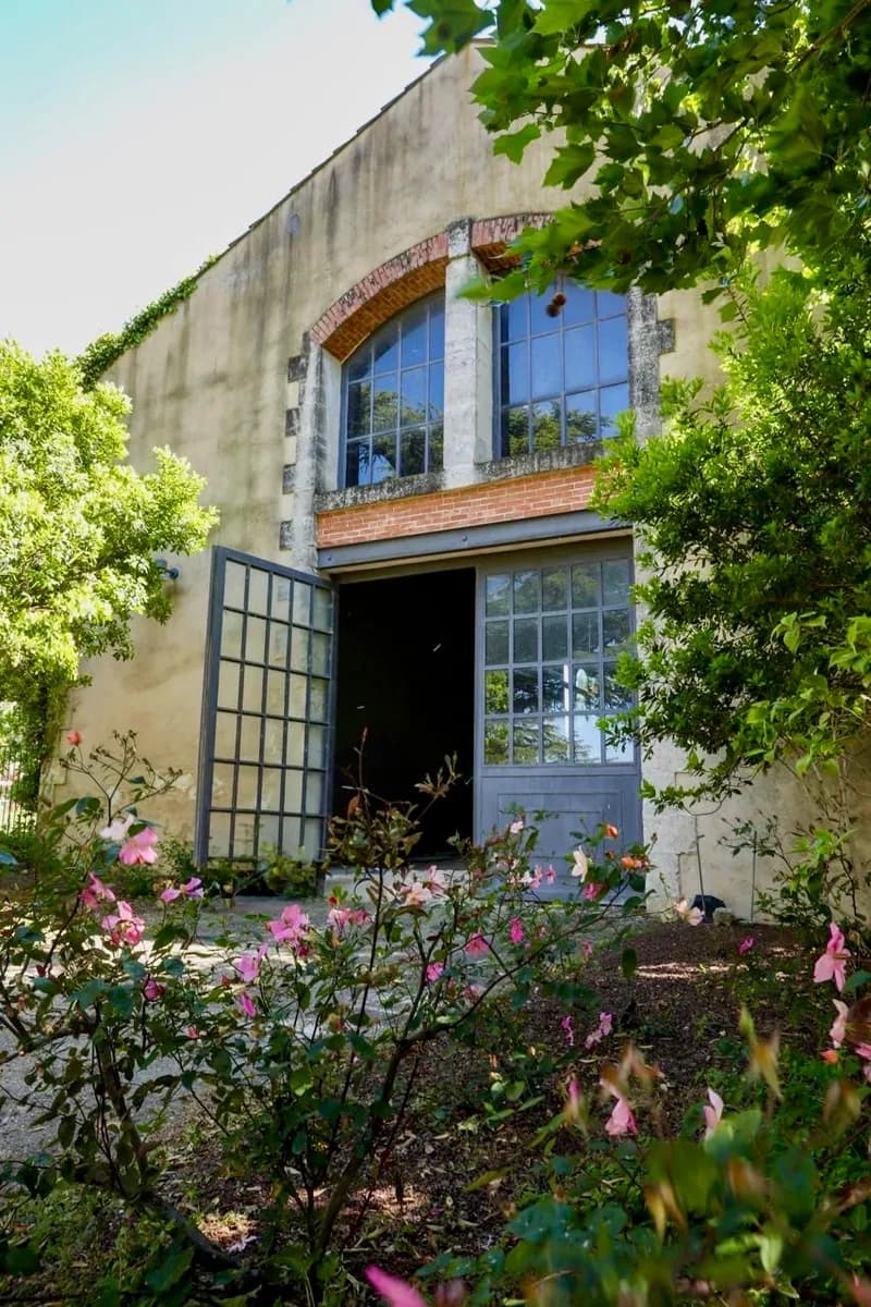 Façade en pierre avec baie cintrée et hautes portes vitrées, bordée de rosiers