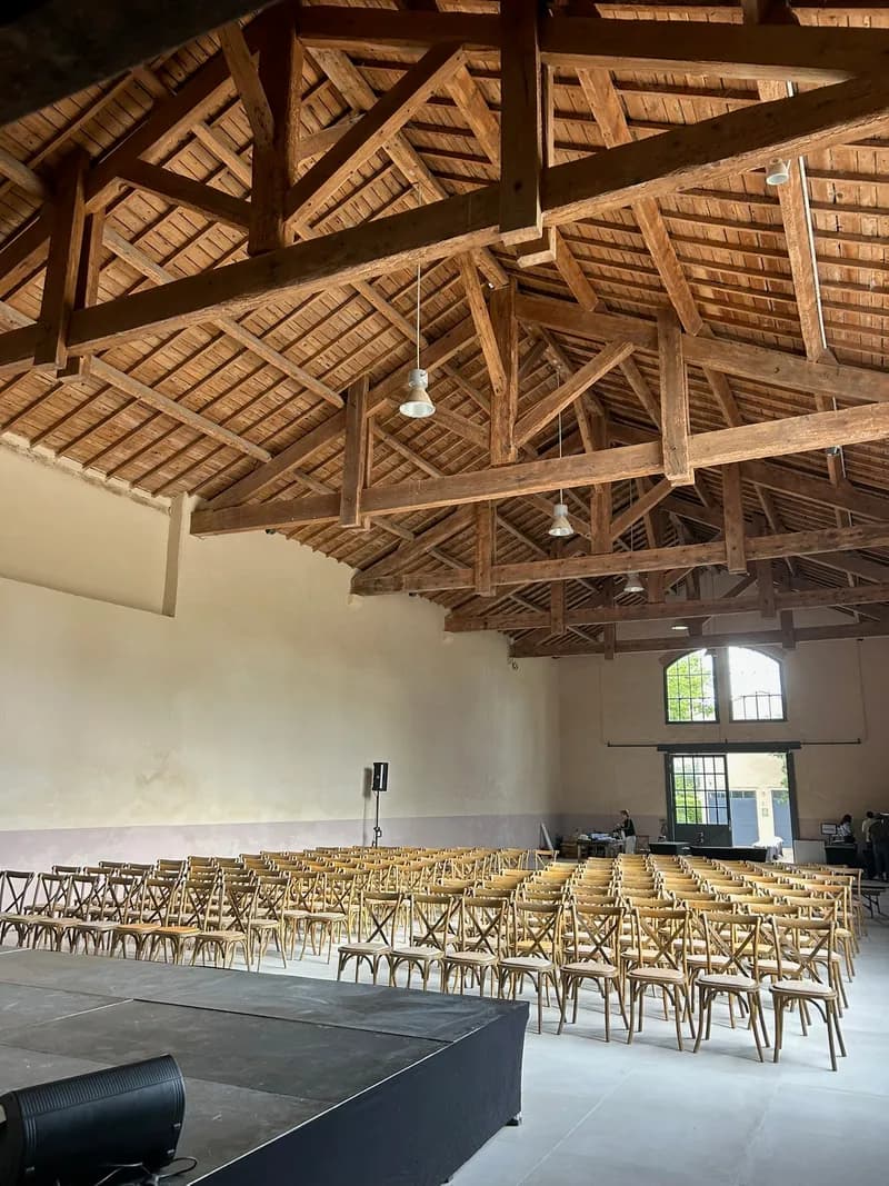 Salle disposée en rangées de chaises face à une scène, sous la charpente en bois