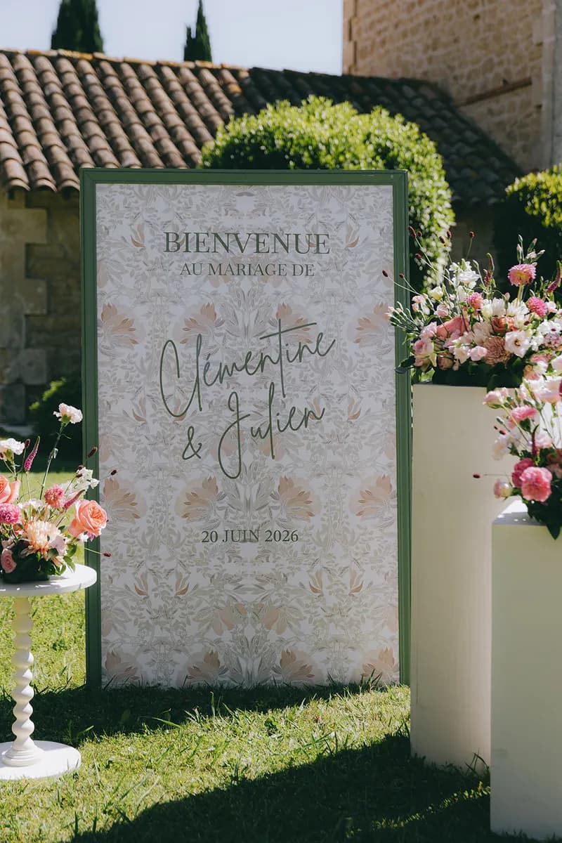 Panneau de bienvenue d'un mariage entouré de compositions florales, sur la pelouse