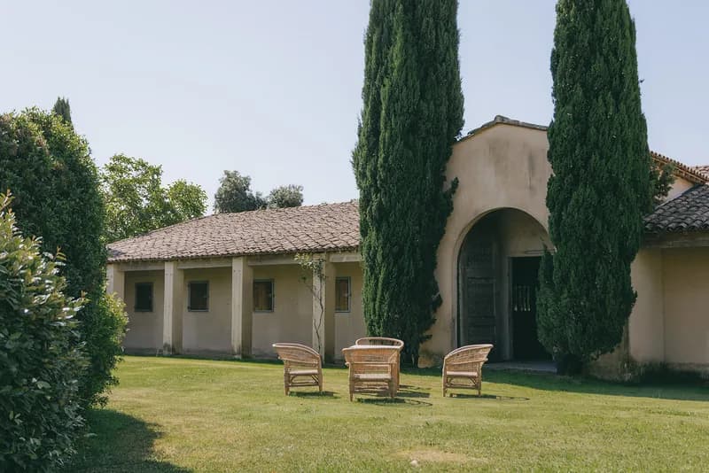 Fauteuils en rotin sur la pelouse devant un bâtiment à porche voûté et cyprès
