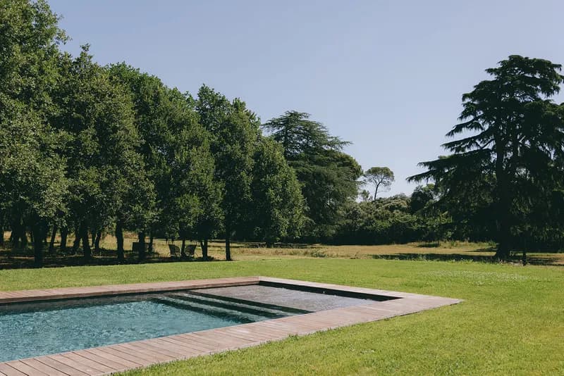 Piscine bordée d'une terrasse en bois, entourée de pelouse et d'arbres