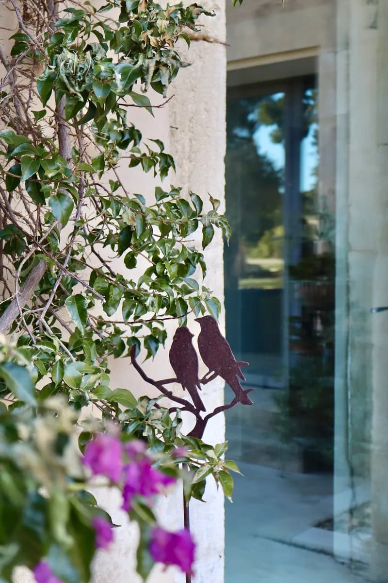 Décor d'oiseaux en métal sur un mur en pierre, parmi le feuillage grimpant