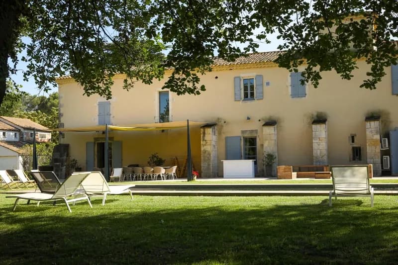 Transats sur la pelouse devant une bâtisse aux volets bleus et sa terrasse ombragée