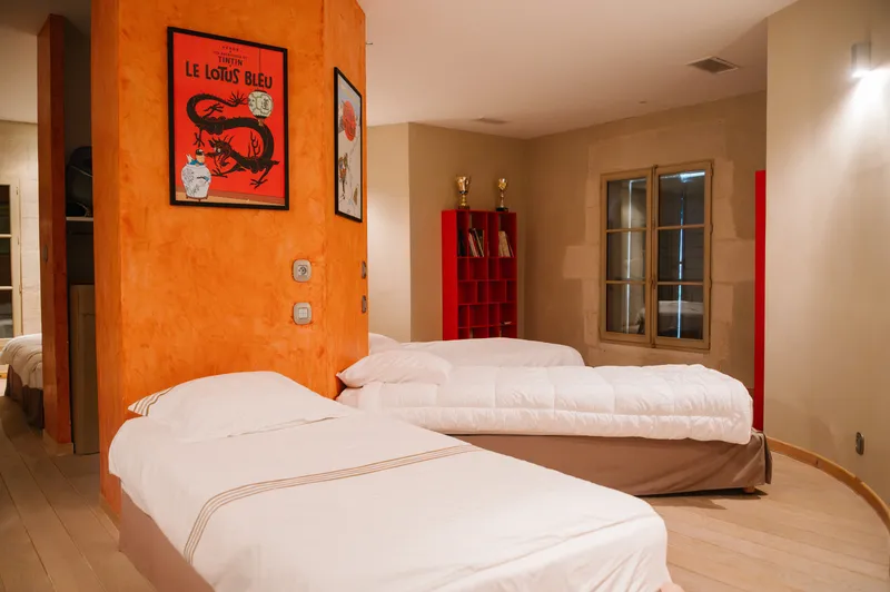 Chambre de trois lits simples, avec mur orangé et affiches encadrées