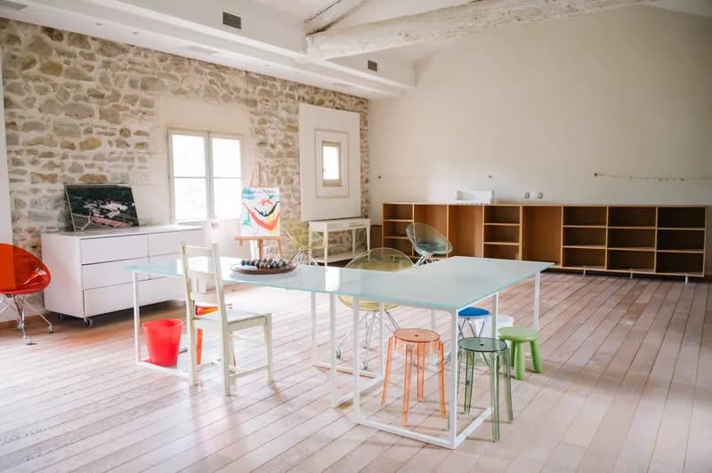 Salle commune avec grande table, tabourets colorés et mur en pierre apparente