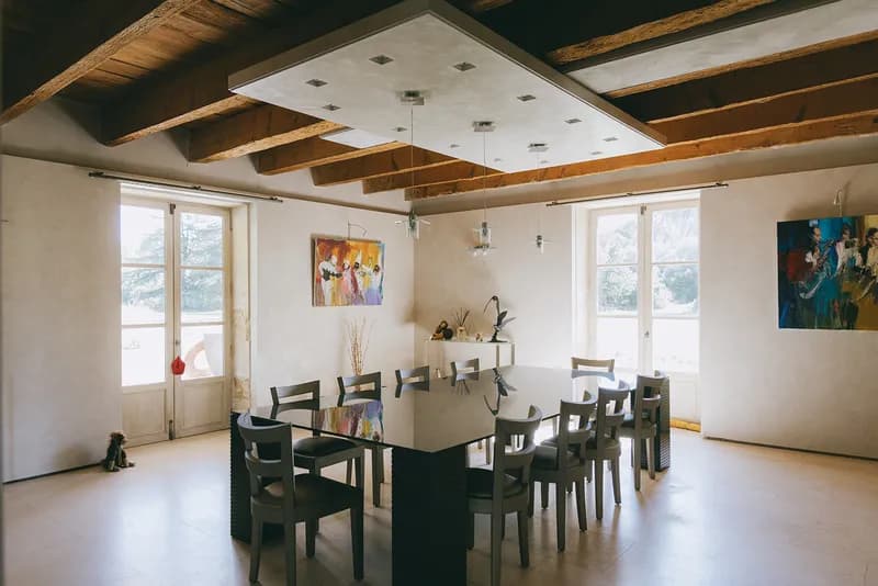 Salle à manger sous poutres apparentes, avec grande table et tableaux colorés