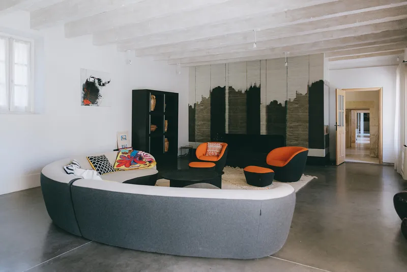 Séjour contemporain avec canapé arrondi et fauteuils orange, sur sol béton