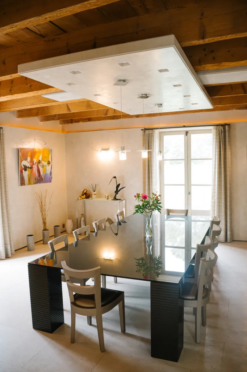 Salle à manger avec grande table, tableau coloré et porte-fenêtre sur le parc