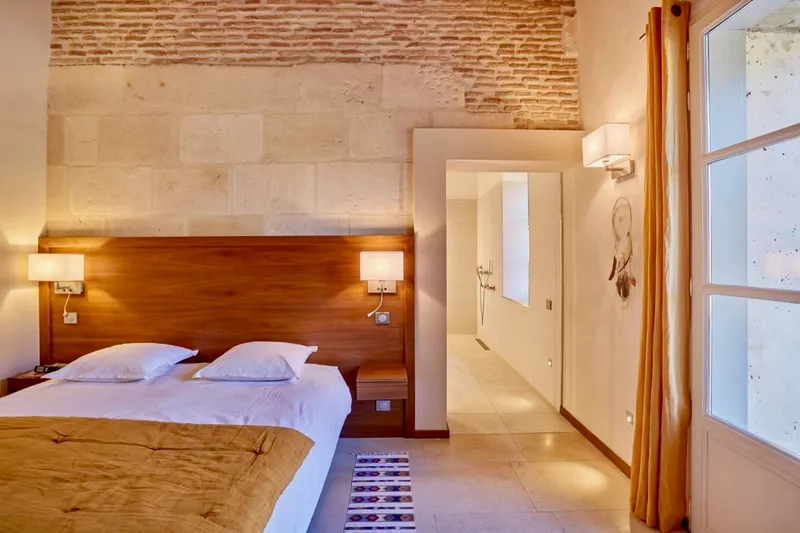 Chambre en pierre avec tête de lit en bois et accès à la salle d'eau
