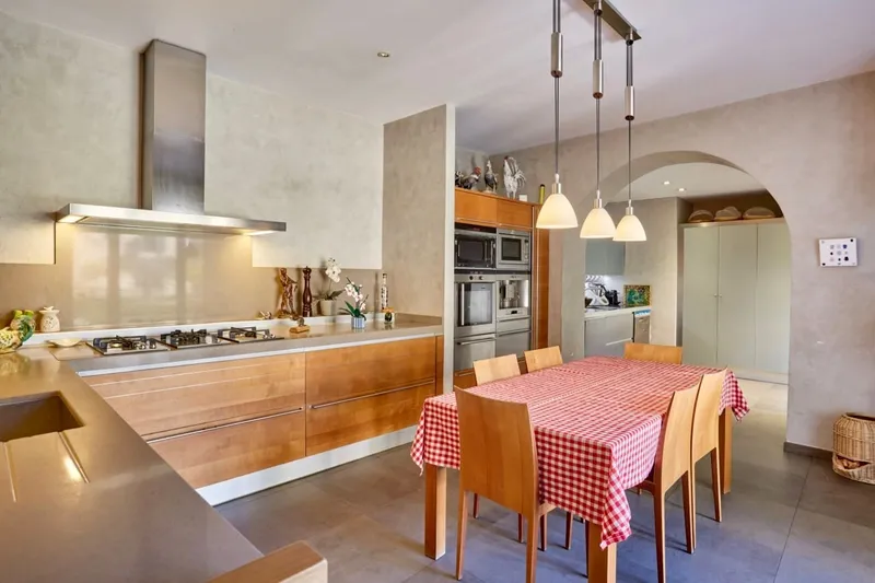 Cuisine équipée avec îlot, hotte inox et table dressée d'une nappe vichy