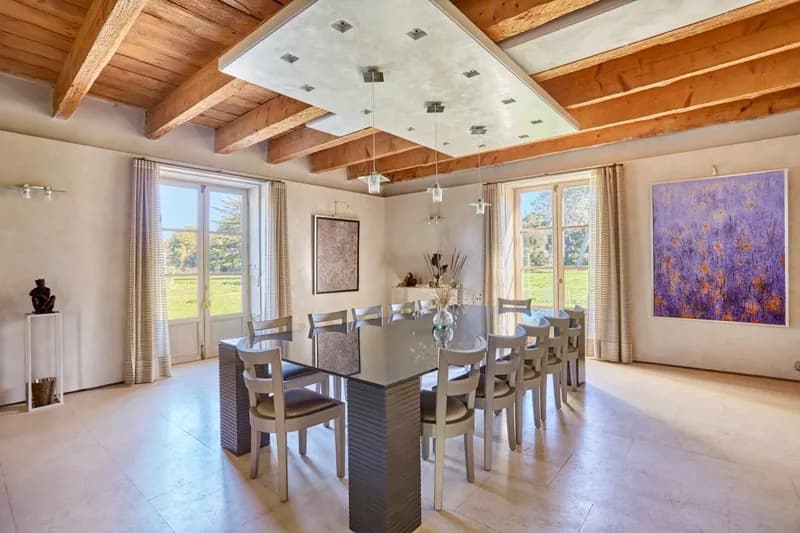 Salle à manger sous poutres claires, ouverte sur le parc par deux portes-fenêtres
