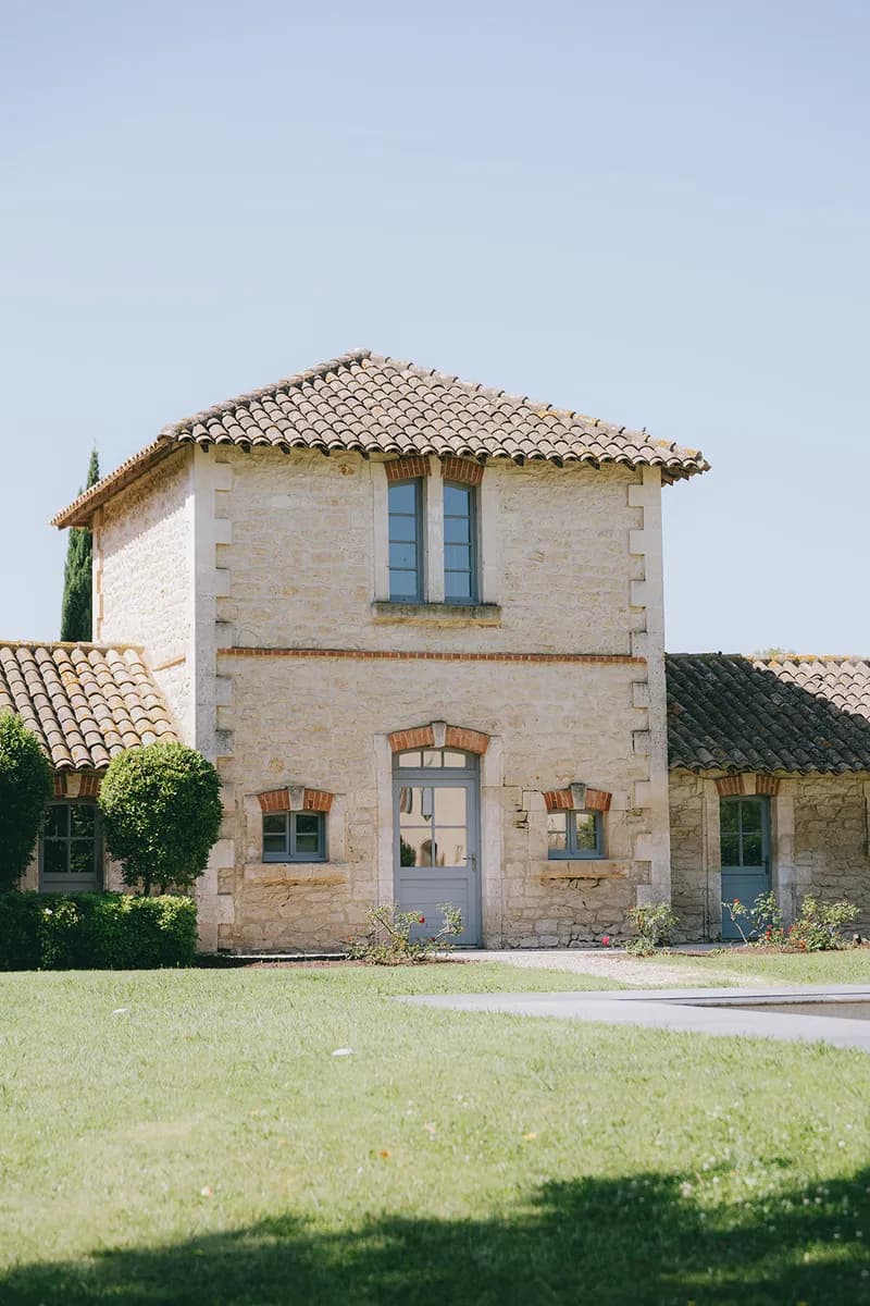 Bâtiment en pierre aux volets bleus, entouré de pelouse et de rosiers